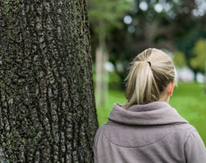 nachdenkliche junge Frau von hinten an Baum gelehnt 