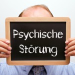 Mann hält sich Schiefertafel mit Aufschrift Psychische Störung vors Gesicht