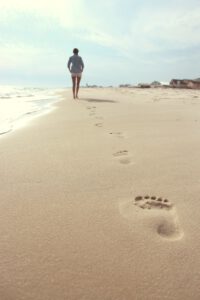 Schritte Fußabdrücke im Sand von Frau, die Richtung Sonne geht